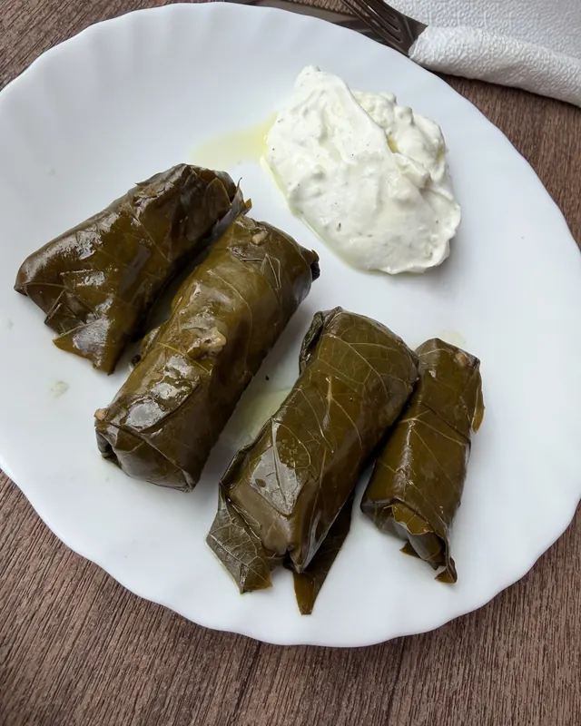 Four sarma, rolled grape leaves, with a spoon of yoghurt